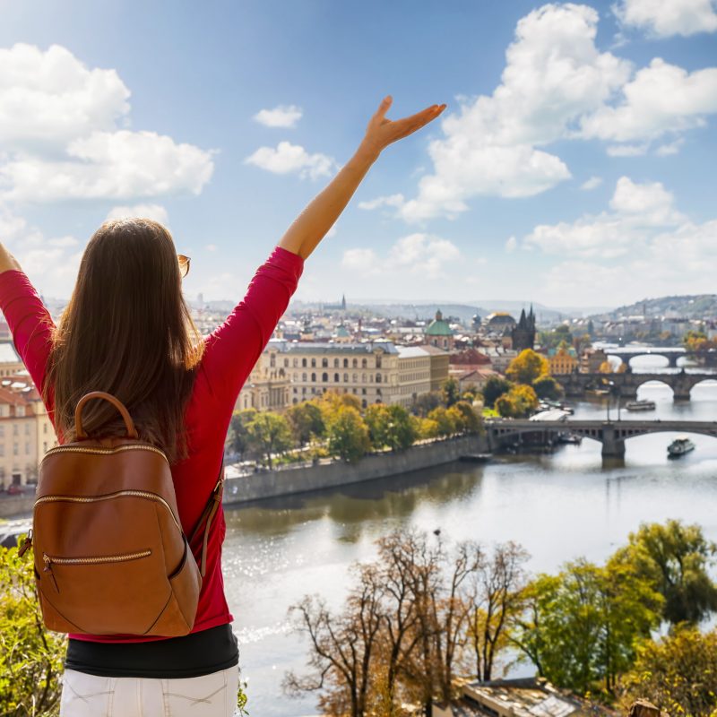 A happy tourist woman enjoys the panoramic view from a hill over the city of Prague, Czech Republic, on a sunny day